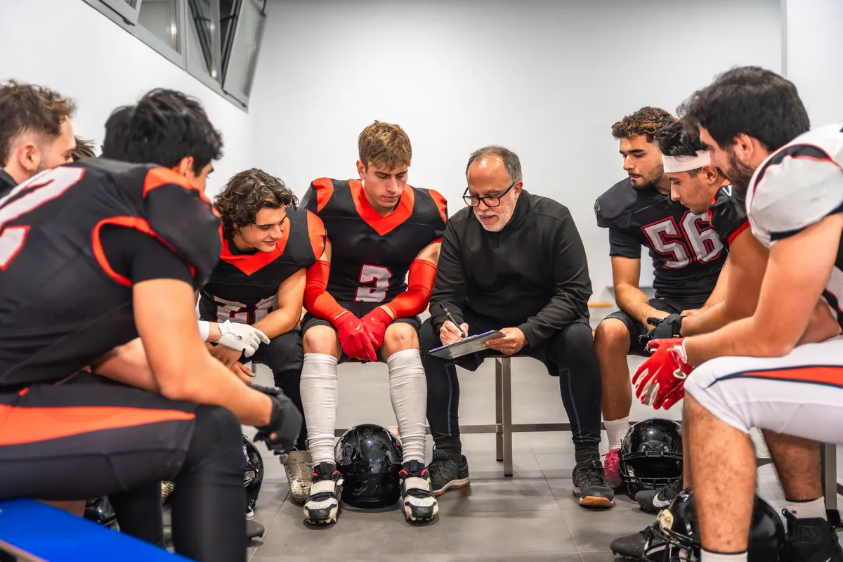 Coach talking to young football players in a locker room