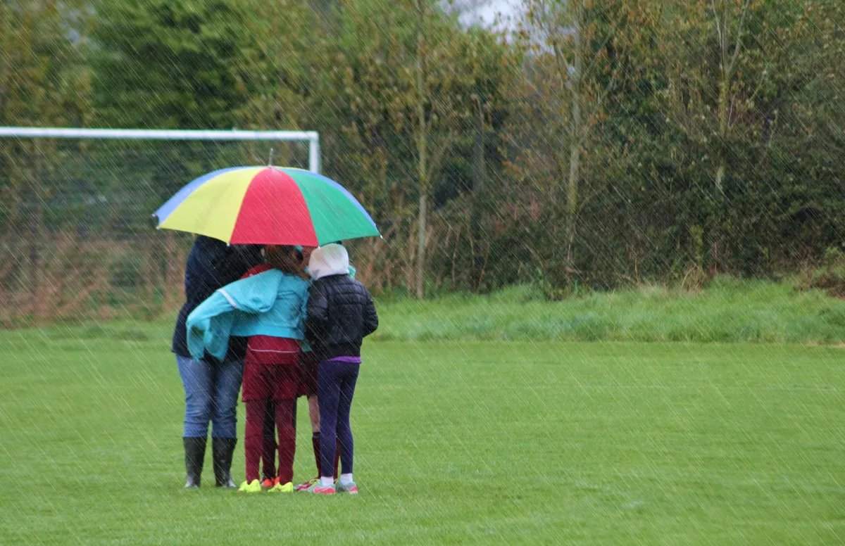 Parents standing under umbrellas at a rainy game day